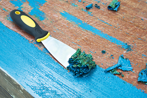 Billede af blå maling, der bliver fjernet fra et træmøbel med en spatel
