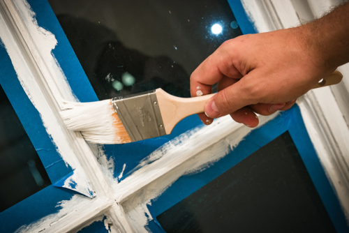 Billede af vindue med blåt malertape, der er i gang med at blive malet hvide