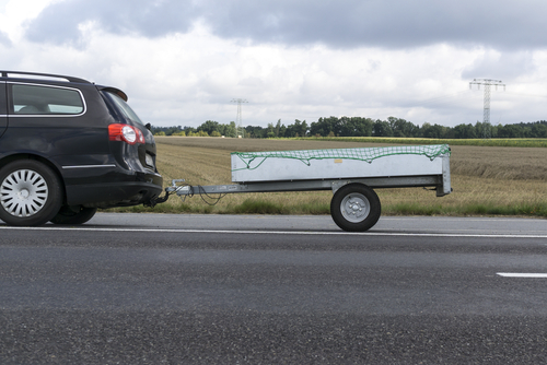 Et billede af en kørende sort bil med trailer på en landevej